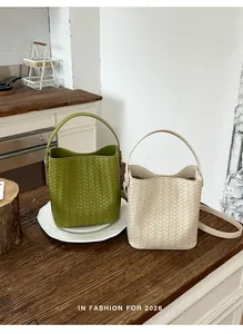 Two stylish woven leather bucket bags in green and beige on a wooden counter