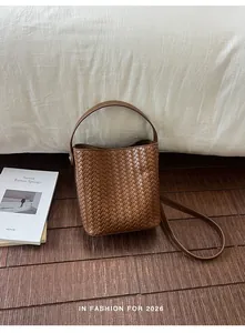 Close-up detail of a brown woven bucket bag on a wooden floor with a white background