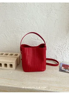 Detailed view of red woven bucket bag featuring top handle in a minimalist studio scene