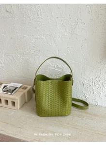 Detail view of a green woven bucket bag on a textured stone surface with natural light.