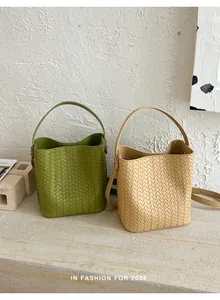 Detail of two woven bucket bags in green and beige featuring detachable cross-body straps