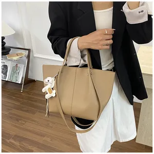 Model holding large tan pebbled leather tote bag with a white puppy charm detail
