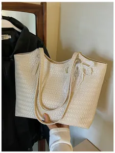 Vue détaillée d'un sac cabas tissé beige tenu à la main avec breloque en dentelle