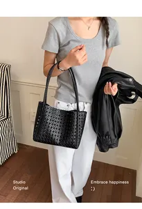 Detail of a black woven leather tote bag carried by a model in a casual outfit