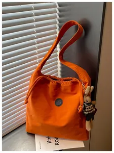 Detail view of the bright orange nylon shoulder bag featuring drawstring and bunny charm