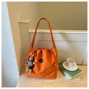 Close-up of vibrant orange nylon bucket bag with cute bunny keychain on a table.