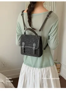 Vista trasera de una modelo con una pequeña mochila gris de fieltro elegante.
