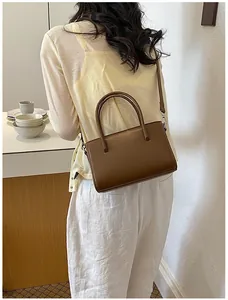 Back view of woman carrying brown rectangular faux leather shoulder bag in style