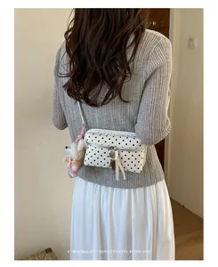 Detail of a white polka dot crossbody bag worn by a model in a minimalist outfit.