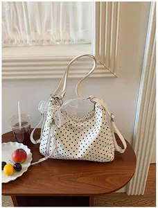 Detailansicht einer weißen Polka-Dot-Tasche mit Perlschleife auf einem kleinen Holztisch.