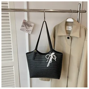 Détail d'un sac cabas tissé noir avec un nœud en dentelle de perles sur un portant.