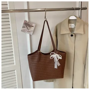 Détail d'un sac cabas tressé marron avec un nœud en dentelle blanche suspendu à un rack.