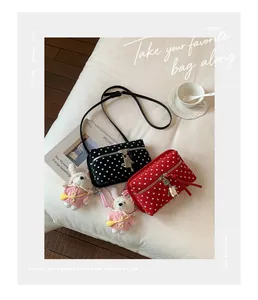 Close-up of black and red polka dot crossbody bags with cute bunny charms on white bed.