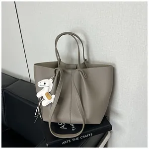 Detailed view of a taupe pebbled leather tote bag with a white horse charm on a sofa