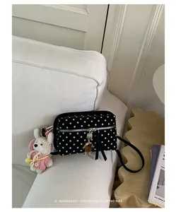 Close-up of a black polka dot crossbody bag with a cute bunny keychain and metal charm.