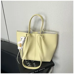 Close-up view of a minimalist pale yellow leather tote bag featuring a cute white dog charm