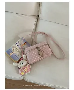 Stylish pink polka dot crossbody bag featuring a cute bunny keychain on a white sofa.