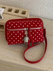 Fashionable red polka dot crossbody bag featuring a unique metal robot charm pendant