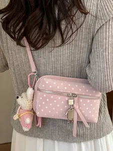 Stylish pink polka dot crossbody bag with cute plush bear and robot charms for women.