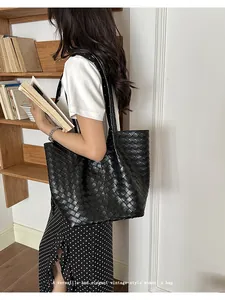 Detail view of a large black woven tote bag worn by a model in a lifestyle setting