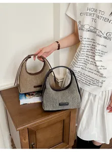 Detailed view of two elegant woven hobo bags in beige and grey on a wooden table.