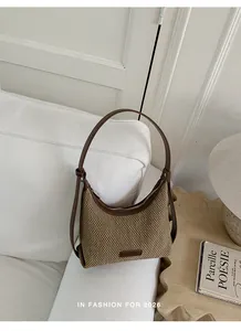 Detailed view of a stylish brown woven croissant shoulder bag placed on a cozy white sofa