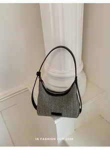 Detail of a minimalist black and white woven dumpling bag on a white pillar background.