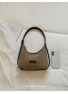 Detailed view of woven croissant shoulder bag with brown leather strap and phone for scale