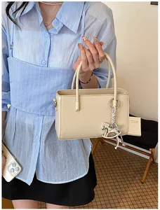 Close-up detail of a minimalist beige handbag featuring a silver rocking horse charm