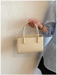 Elegant cream handbag being held, showing smooth leather texture and minimalist design.