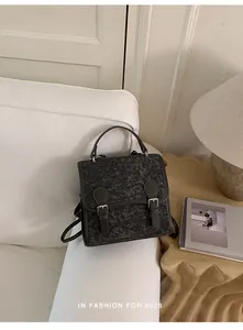 Vista detallada de una mochila de mezclilla gris con detalles en cuero marrón y asa.