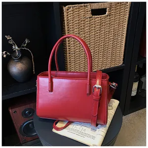 Elegant red leather handbag with top handles and shoulder strap in a cozy room setting.