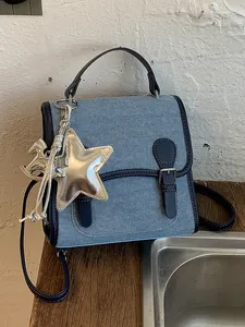Mochila ligera de mezclilla para mujer con dije de estrella plateada y cierre de hebilla.