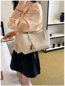 Élégant sac cabas tressé crème avec pendentif en perles colorées porté par un mannequin