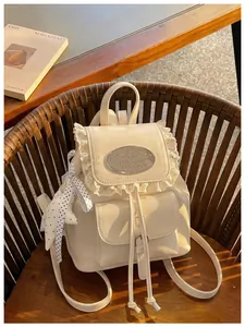 Detail view of a cream white vintage mini backpack featuring lace trim and a metal plaque