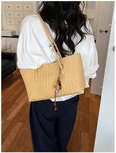 Vue détaillée d'un sac cabas tissé beige avec charme coloré sur l'épaule du modèle.