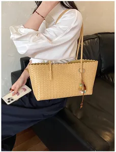 Détail d'un grand sac fourre-tout tissé beige avec un charme coloré porté par un mannequin.