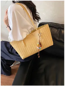 Sac cabas en paille tissée chic avec breloque colorée, porté à l'épaule avec style.