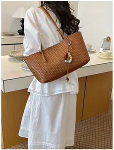 Détail d'un sac cabas tressé marron porté par un mannequin dans un café élégant