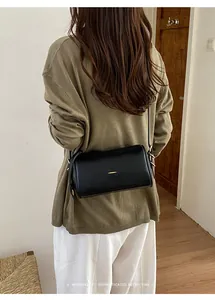 Ein Mode-Modell trägt eine schwarze minimalistische Boston-Tasche im Retro-Stil.