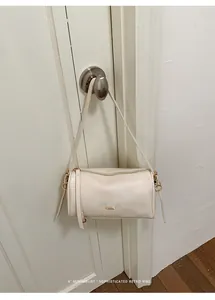 Elegante cremeweiße minimalistische Zylindertasche mit Goldakzenten an einer Tür