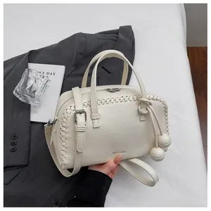 Close-up of cream Boston handbag with woven details and round charms on a grey blazer.