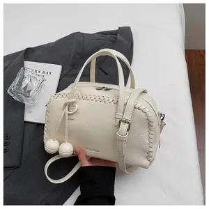 Detailed shot of a cream-colored Boston handbag with woven edges and decorative ball charms