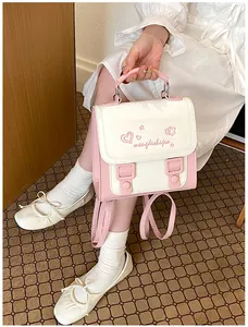 Fashionable pink and white small backpack for women shown held by top handle in lifestyle setting