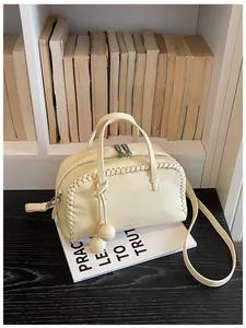 Detail view of cream Boston bag with whipstitch trim and textured leather on a white book.