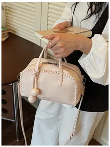 Detail view of a pink pebbled leather Boston bag with whipstitch trim and ball charms.