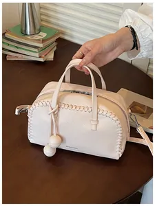 Close-up of a pink pebbled leather Boston bag with woven stitch details and ball charms
