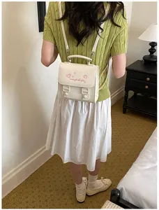 Back view of a model wearing a small cream faux leather backpack with pink embroidery