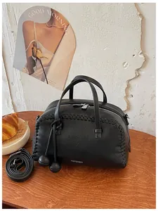 Detail view of a black Boston handbag with litchi grain texture and braided stitching