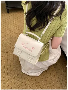 Back view of a stylish white mini backpack with pink heart embroidery on a green top
